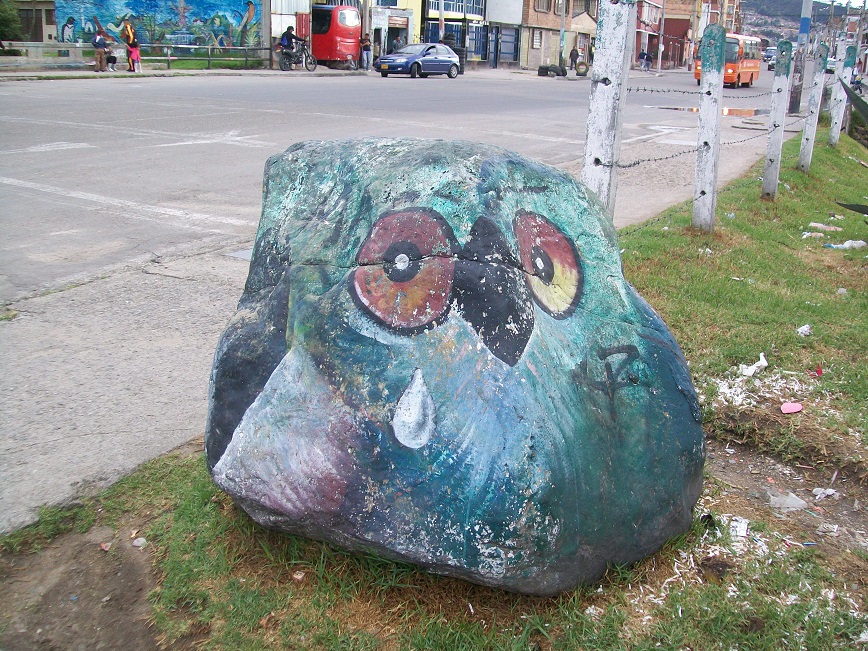 the rock is painted green, with the eyes and beak of a bird, and a teardrop coming from one eye